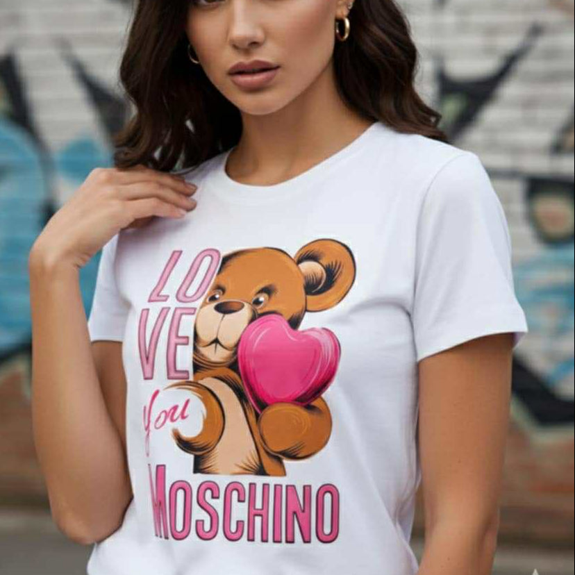 Момиче с бяла тениска Love Moschino с голям цветен принт на мече, държащо розово сърце, и надпис Love You.