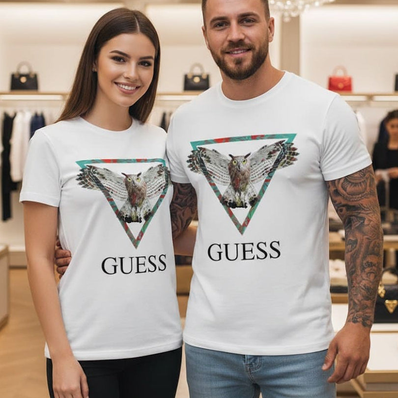Мъж и жена позират в луксозен магазин с еднакви бели тениски с надпис Guess и графика на разперила криле сова в триъгълник.
