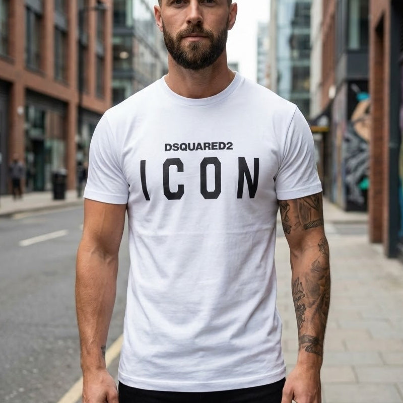 Мъж с татуировки носи бяла тениска DSQUARED2 с голям черен надпис ICON на гърдите.
