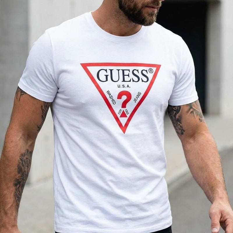 Мъж с бяла тениска Guess с голямо триъгълно лого и татуировки