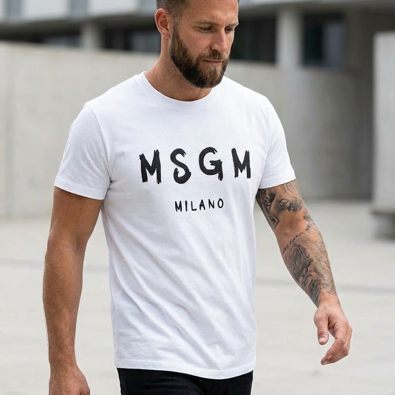 Мъж с бяла тениска MSGM с черен ръкописен надпис Milano и татуировки