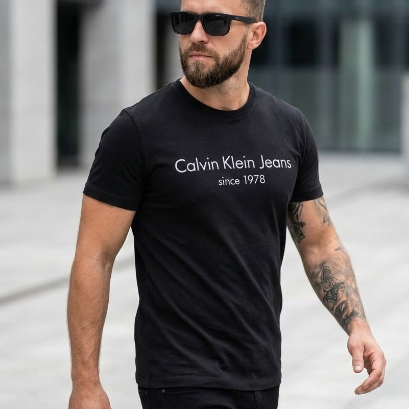 Мъж със слънчеви очила и черна тениска Calvin Klein Jeans с бял надпис since 1978