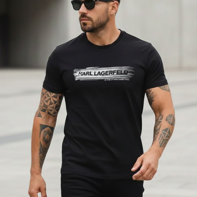 Мъж с татуировки, носещ черна тениска Karl Lagerfeld с бяло графично лого и слънчеви очила.
