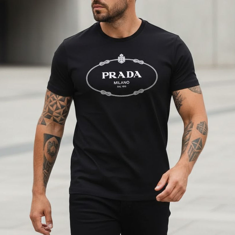 Мъж със стилна прическа и татуировки, облечен в черна маркова тениска Prada с бяло овално лого.