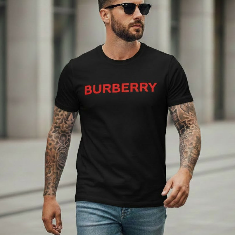 Мъж с татуировки и слънчеви очила, облечен в черна тениска с червен надпис Burberry и дънки.