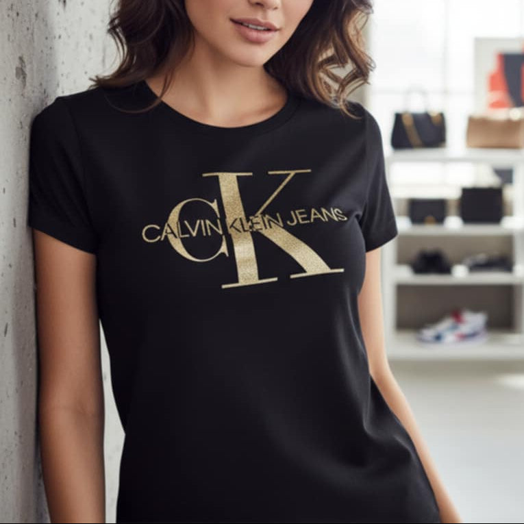 Млада жена, позираща с черна тениска Calvin Klein Jeans, отличаваща се с голямо лого cK в блестящ златист цвят.