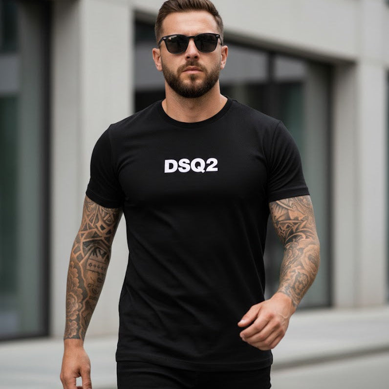 Мъж в черна тениска с къс ръкав и бял графичен надпис DSQ2 на гърдите, ходещ по градска улица.