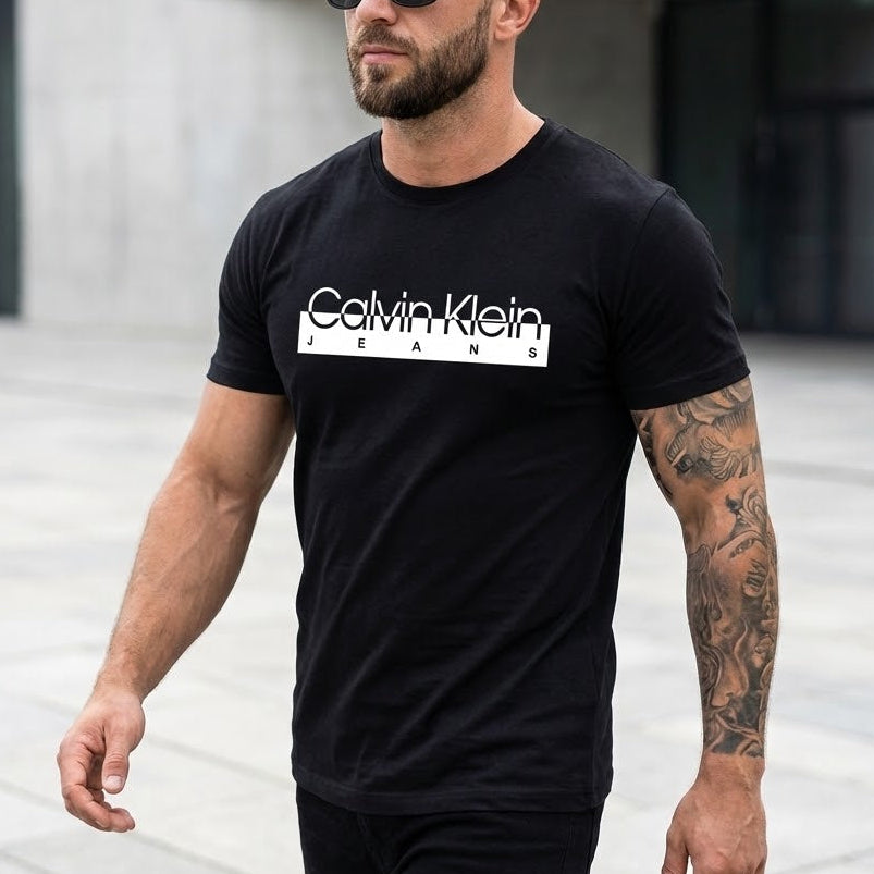 Мъж с черна тениска Calvin Klein Jeans с модерно бяло лого в центъра и татуировки